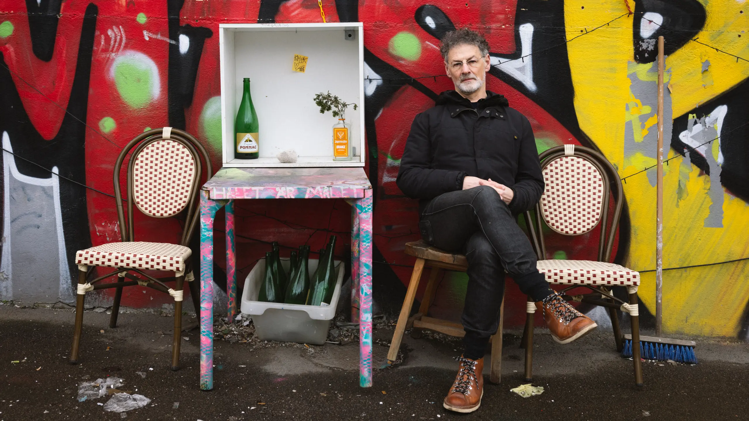Konstnären Bogdan Szyber på en stol framför en färgglad graffitivägg.
