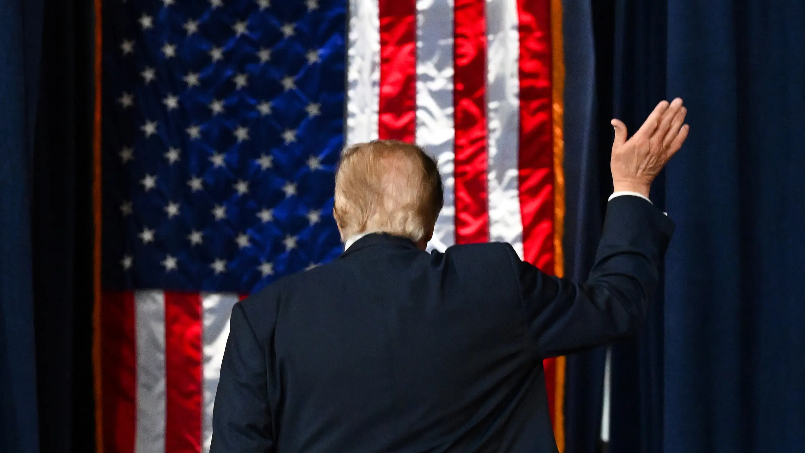 Donald Trump bakifrån, med amerikansk flagga i bakgrunden.